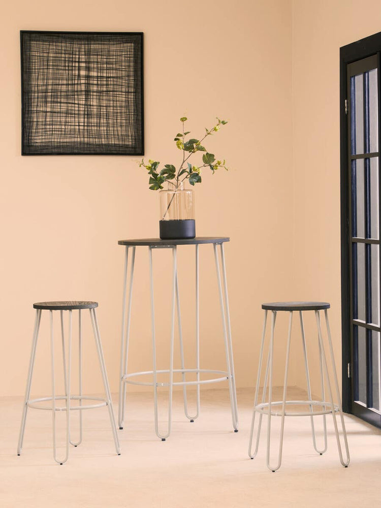 Three-piece bar table and stool set featuring a sleek elm wood tabletop and two matching stools with wooden seats. The table stands on slender metal legs, and a small potted plant is placed on the table. The background includes a light-colored wall and a window with black frames, creating a modern and inviting atmosphere