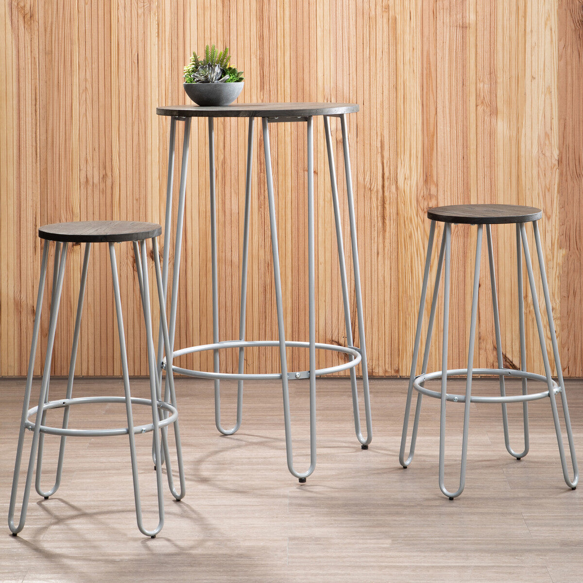 A three-piece bar table and stool set featuring a tall, slender elm wood table with a natural finish and sleek metal legs, accompanied by two matching stools with round seats and metal frames. A small potted plant sits on the table, and the background consists of wooden paneling, creating a warm and inviting atmosphere