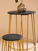 A modern bar table and two stools featuring a sleek gold finish with thin, geometric legs. The table has a round black top, while one stool is slightly smaller and also has a black seat. A decorative glass vase sits on the table, adding a touch of elegance to the set against a soft beige background