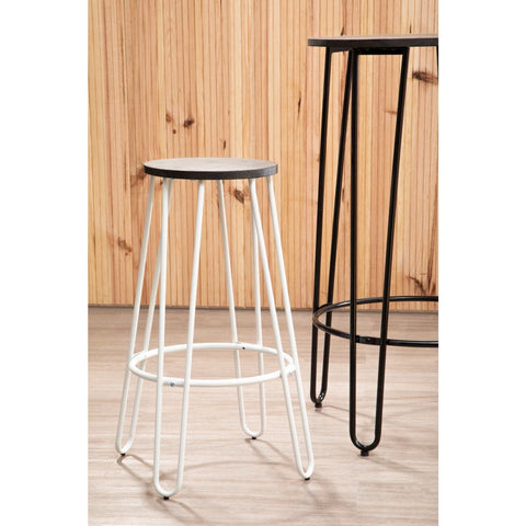 A white finish metal frame bar stool with a round black seat, featuring slender legs and a minimalist design, positioned next to a taller black metal bar table against a wooden backdrop