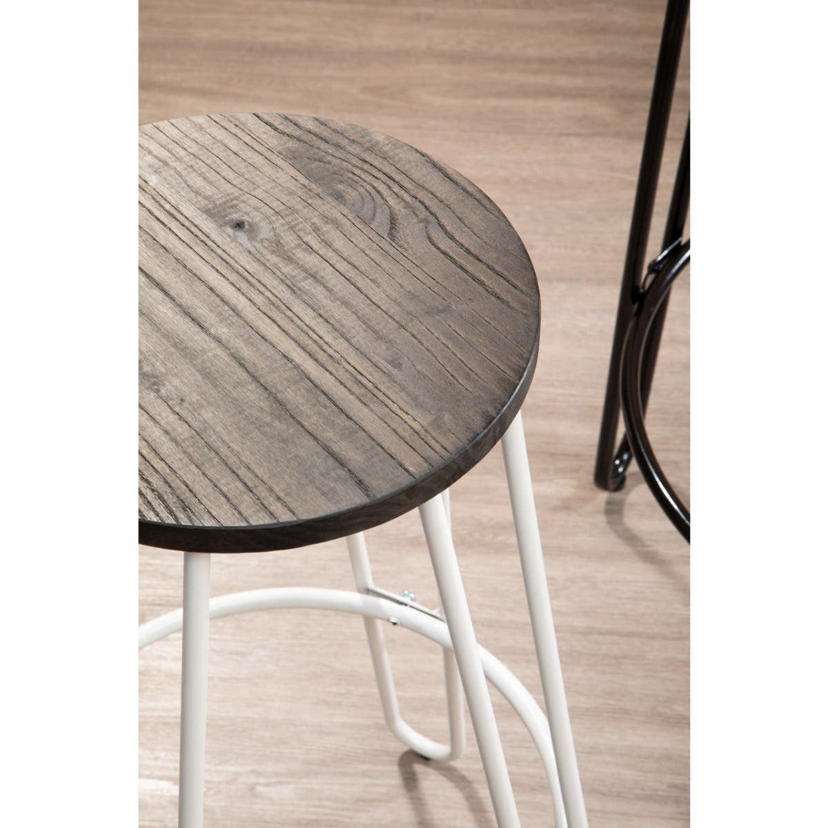A close-up view of a bar stool featuring a round wooden seat with a rustic finish and a white metal frame. The stool is positioned on a light-colored wooden floor, highlighting its modern design and contrasting materials