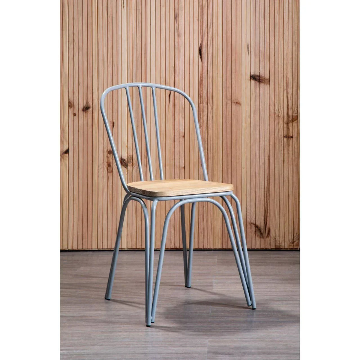 Metal dining chair with light wood seat against wooden panel wall on laminate floor