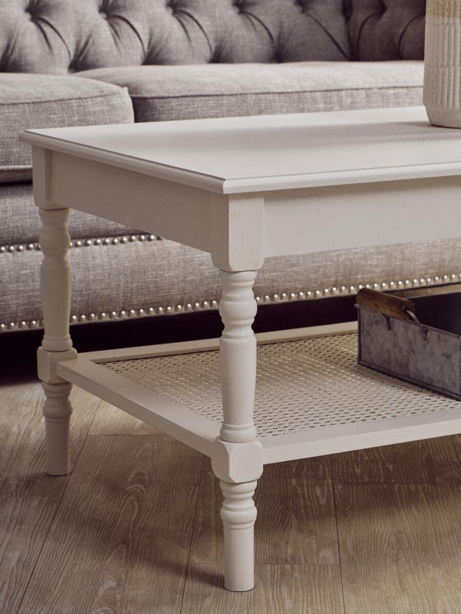 White wooden coffee table with turned legs and lower rattan shelf on wood flooring