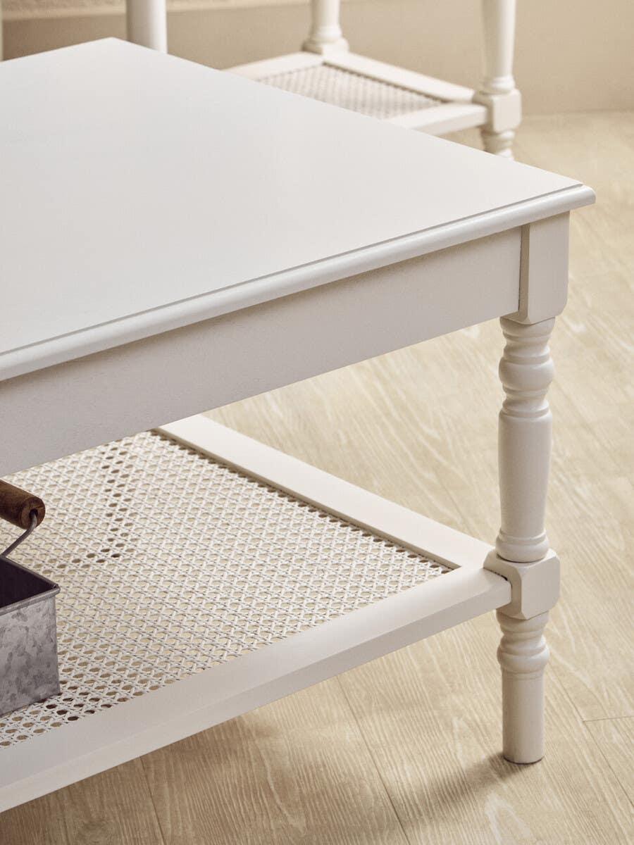 White coffee table with turned legs and woven rattan lower shelf on wood floor