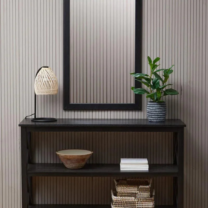 Black console table with rattan lamp, plant, baskets, and wall mirror in hallway setting