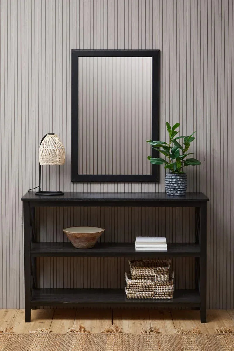Black console table with rattan lamp, plant, baskets, and wall mirror in hallway setting