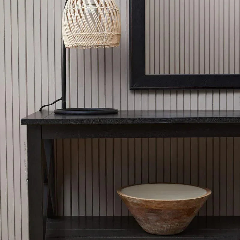 Black console table with rattan table lamp and decorative wooden bowl against striped wall
