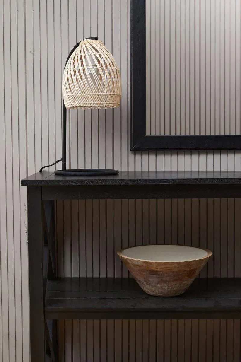 Black console table with rattan table lamp and decorative wooden bowl against striped wall