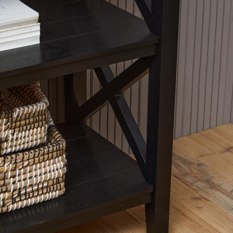 Black wooden shelving unit with cross detail, stacked baskets, and books on lower shelves