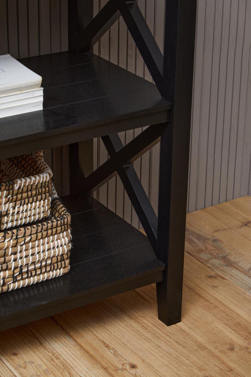 Black wooden shelving unit with cross detail, stacked baskets, and books on lower shelves