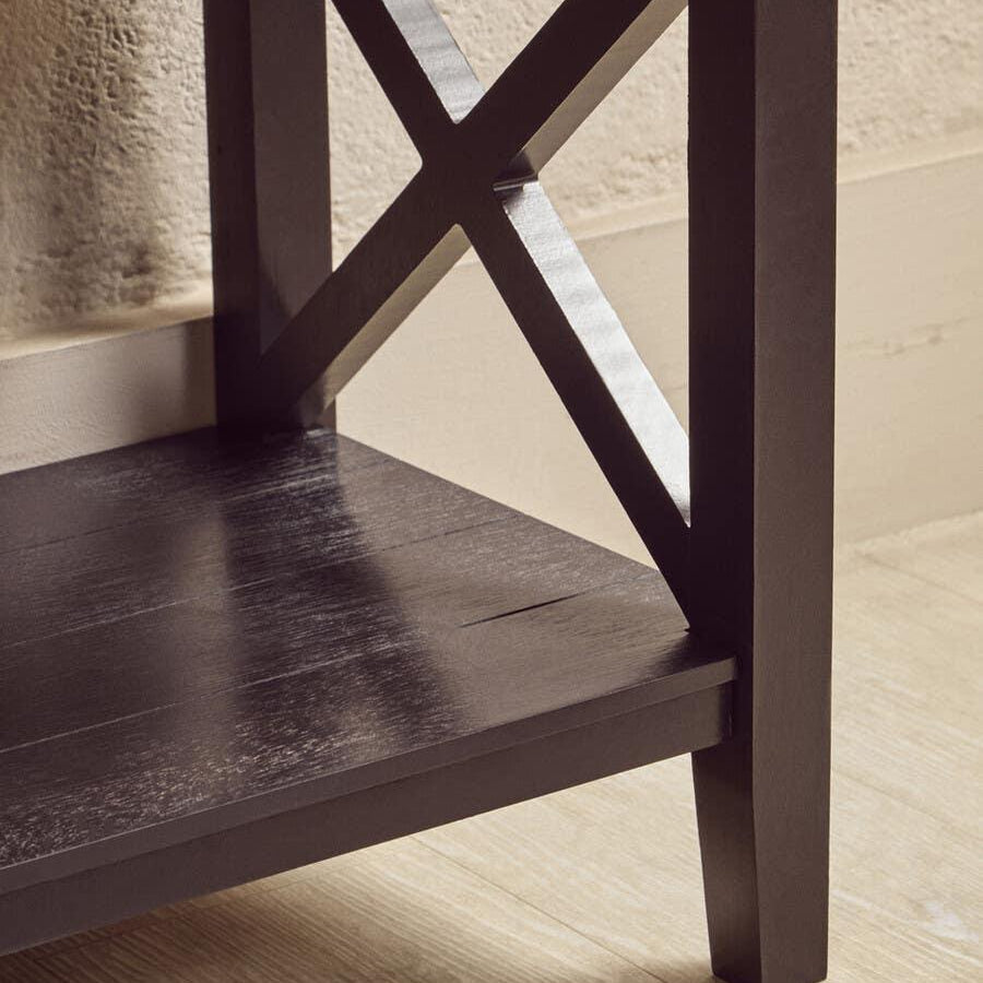 Dark wood furniture leg with X-frame detail and lower shelf on light flooring