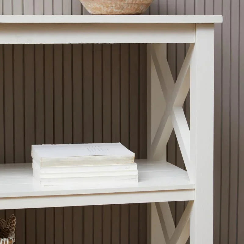 White wooden shelving unit with cross side detail, wooden bowl, stacked books, wicker baskets