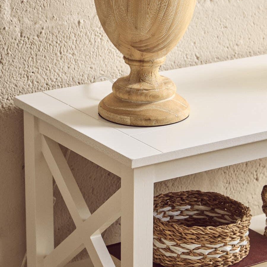 White wooden console table with X side detail, wicker basket, books, and wood lamp base