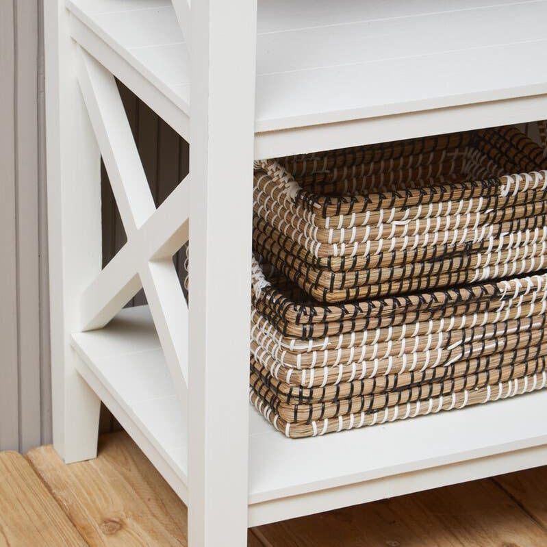 White wooden shelving unit with lower shelf holding stacked woven storage baskets