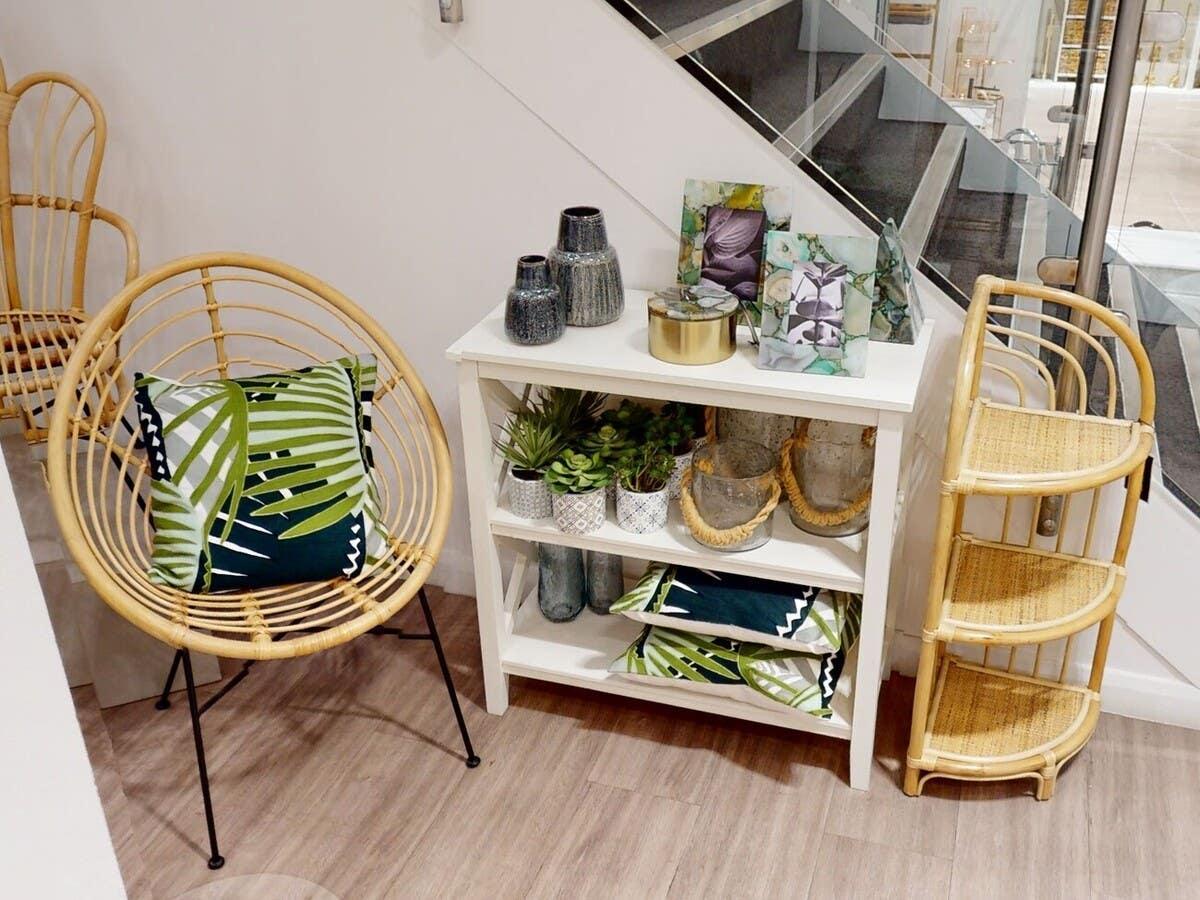 Rattan accent chair with green leaf cushion and white shelf with decorative home accessories