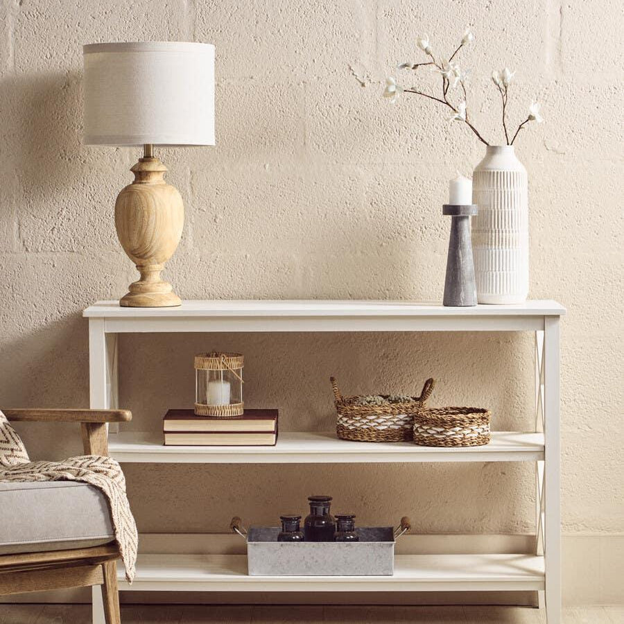 White console table with shelves, styled with lamp, vases, books and woven baskets