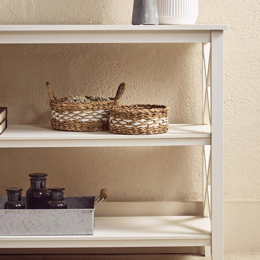 White console table with decorative baskets and metal tray on wooden floor