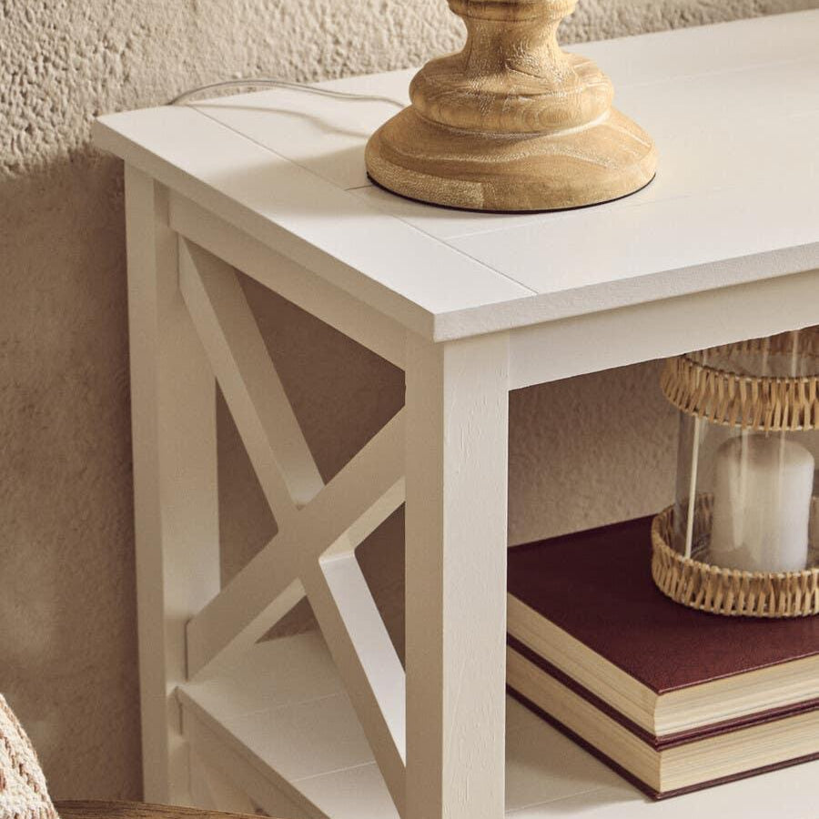 White wooden console table with cross detail, stacked books and decorative lamp