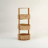 Three-tier storage caddy made from water hyacinth, featuring a natural woven texture and a sturdy handle on top for easy carrying. Each tier consists of round, open baskets, providing a stylish and functional storage solution. The caddy is set against a light, neutral background
