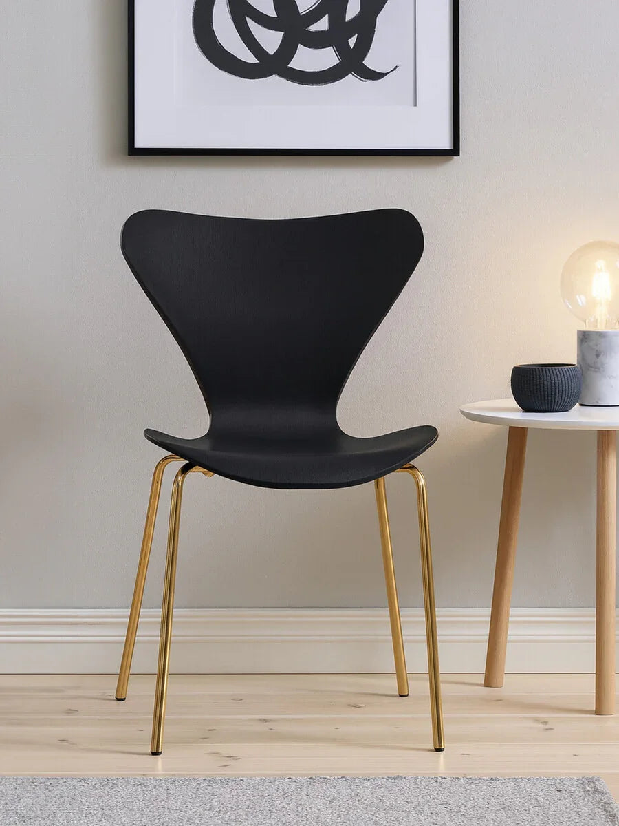 Black modern dining chair with curved seat and gold metal legs beside a round white table