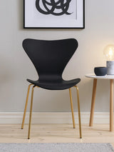 Black modern dining chair with curved seat and gold metal legs beside a round white table