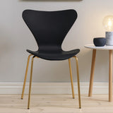 Black dining chair with gold metal legs beside round white side table on wooden floor