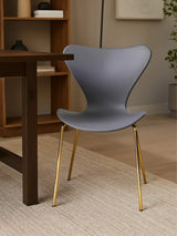 Grey dining chair with gold metal legs beside dark wood table on beige rug