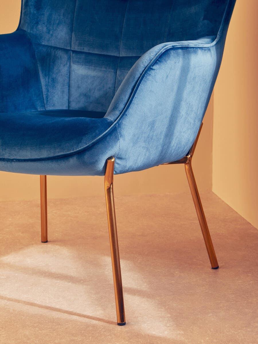 Blue velvet accent chair with gold metal legs, angled view against neutral background