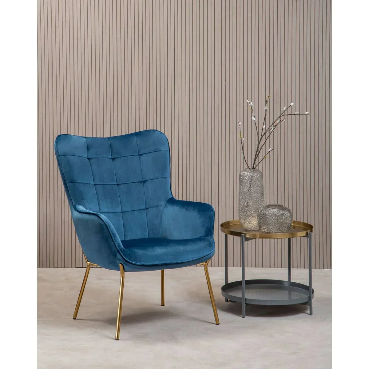 Blue velvet accent chair with gold legs beside round side table and decorative vases