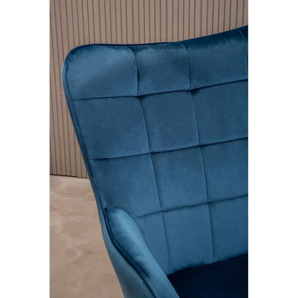 Blue velvet accent chair with grid-stitched backrest, shown close-up against modern panel wall