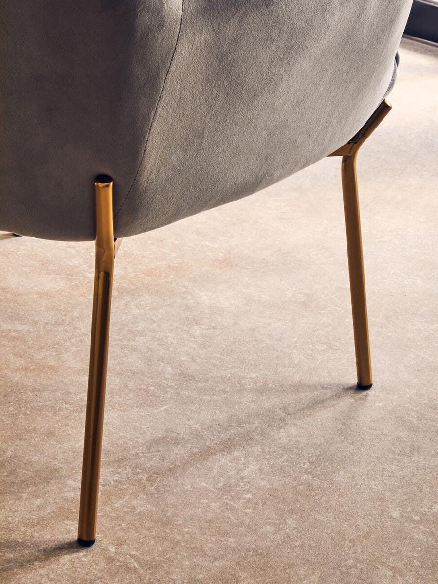 Grey upholstered chair with slim gold metal legs on beige carpet