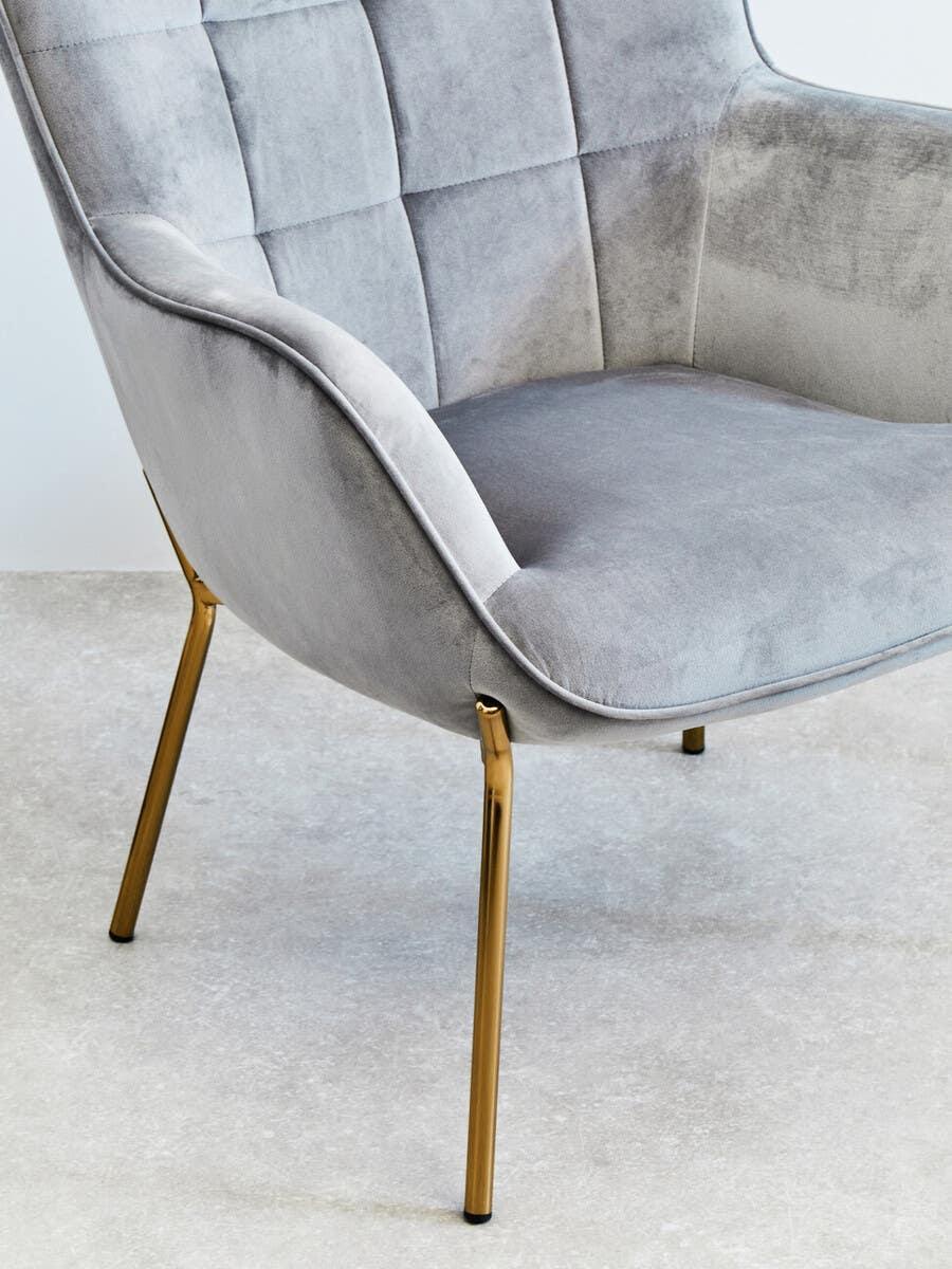 Grey velvet accent chair with gold metal legs and quilted backrest on light floor