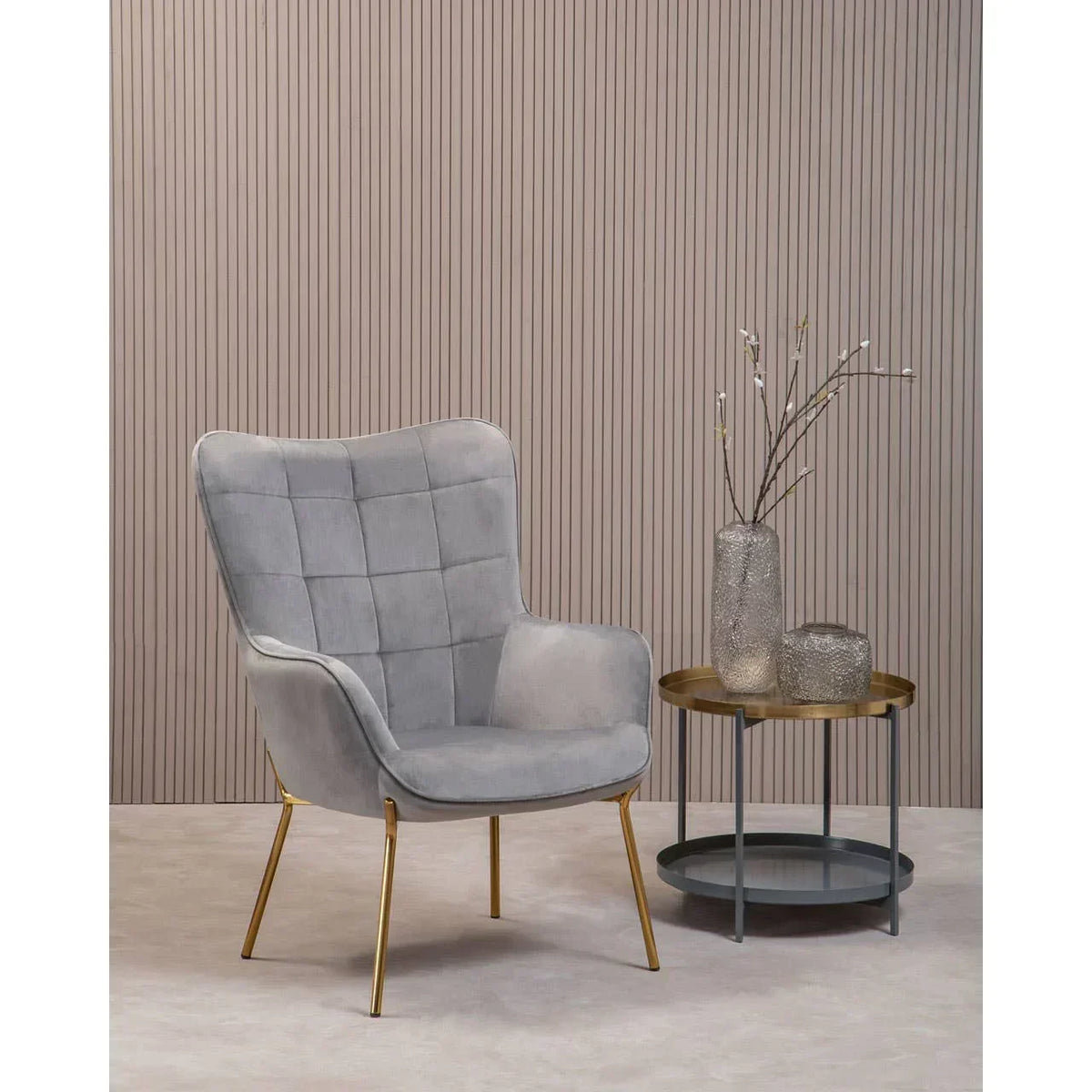 Grey accent chair with gold legs beside round side table with glass vases