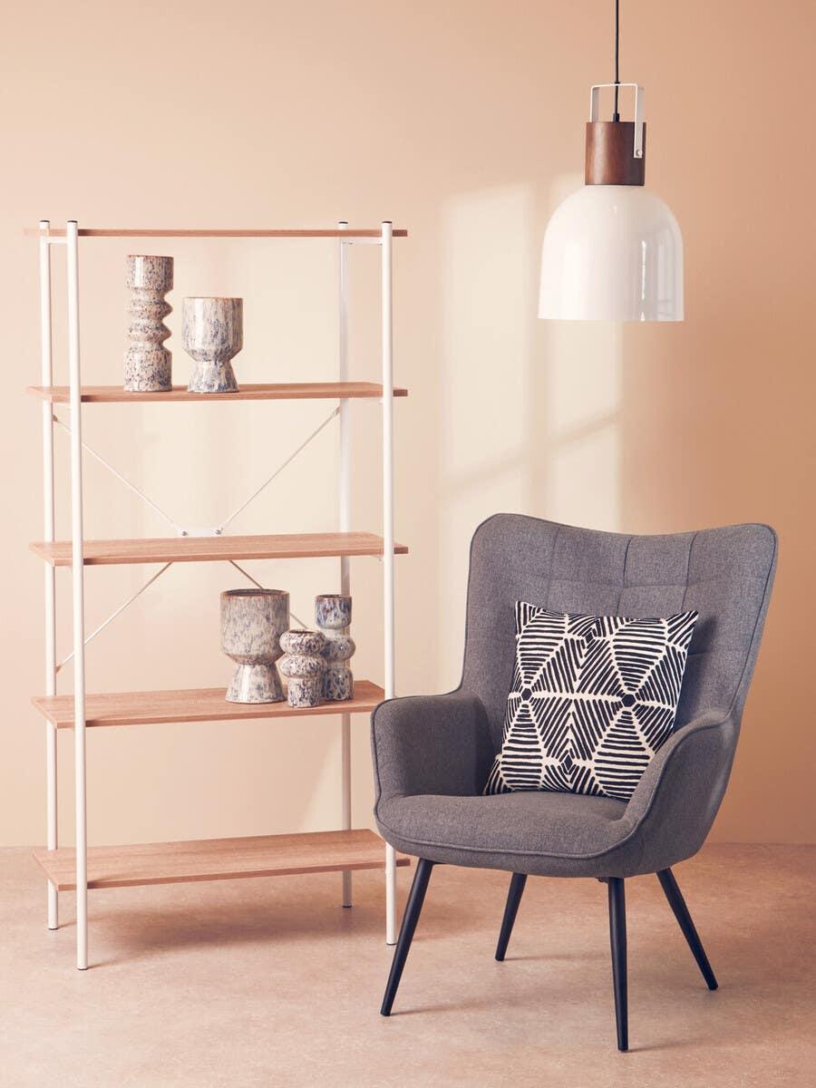 Grey accent chair with patterned cushion beside wooden shelving unit and modern pendant light