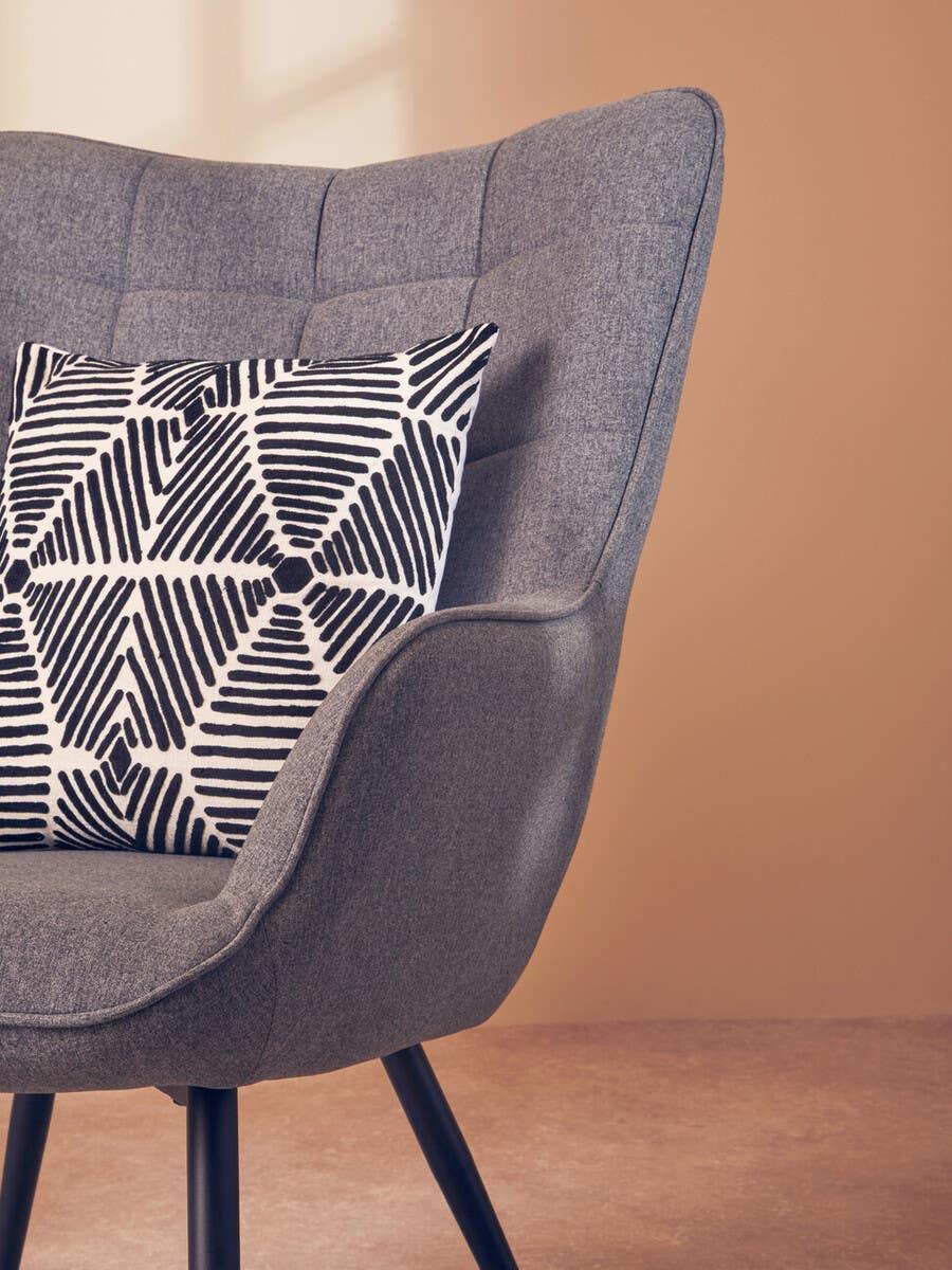 Grey upholstered accent chair with black metal legs and geometric cushion