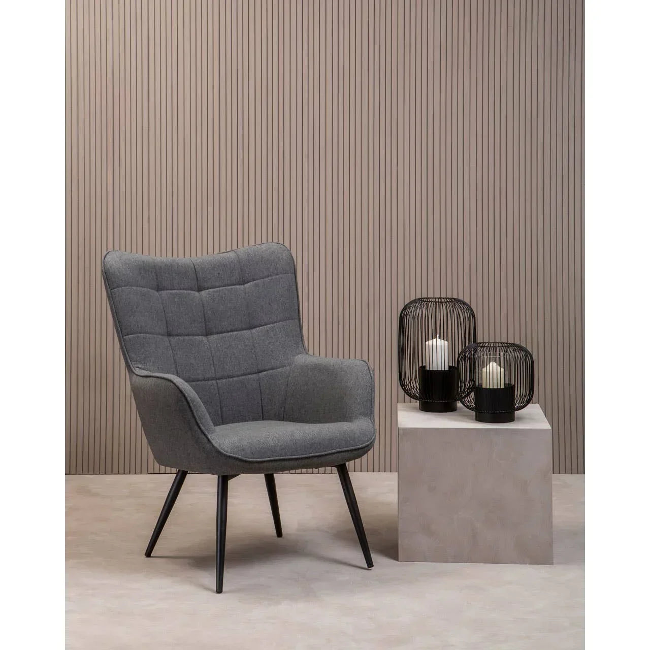 Grey fabric accent chair with black legs beside modern candle holders on cube table