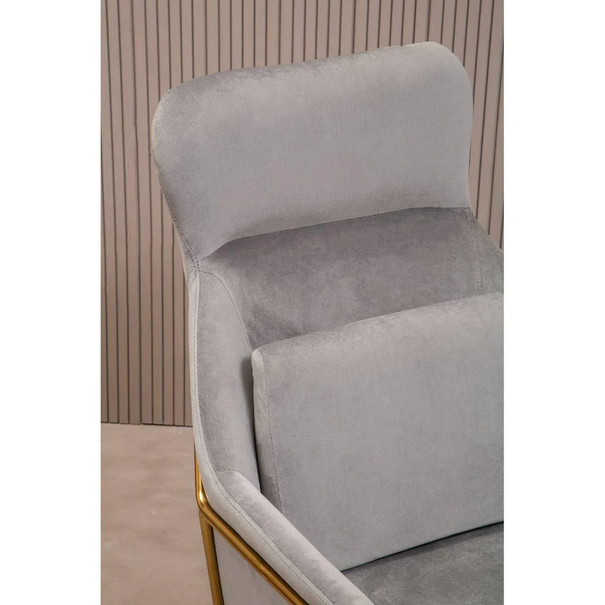 Grey velvet armchair with gold metal frame and plump cushion, close-up angled view