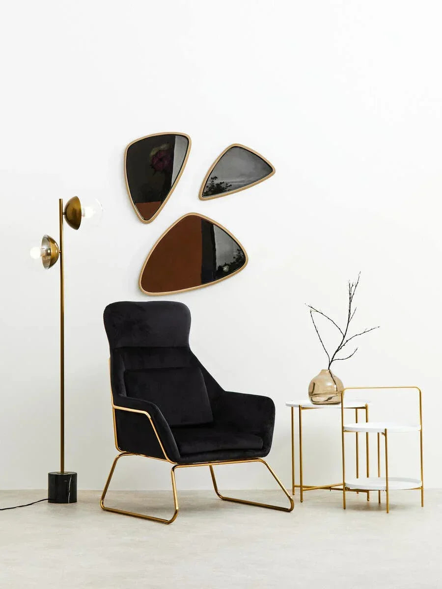 Black velvet accent chair with gold frame beside marble side tables and modern floor lamp