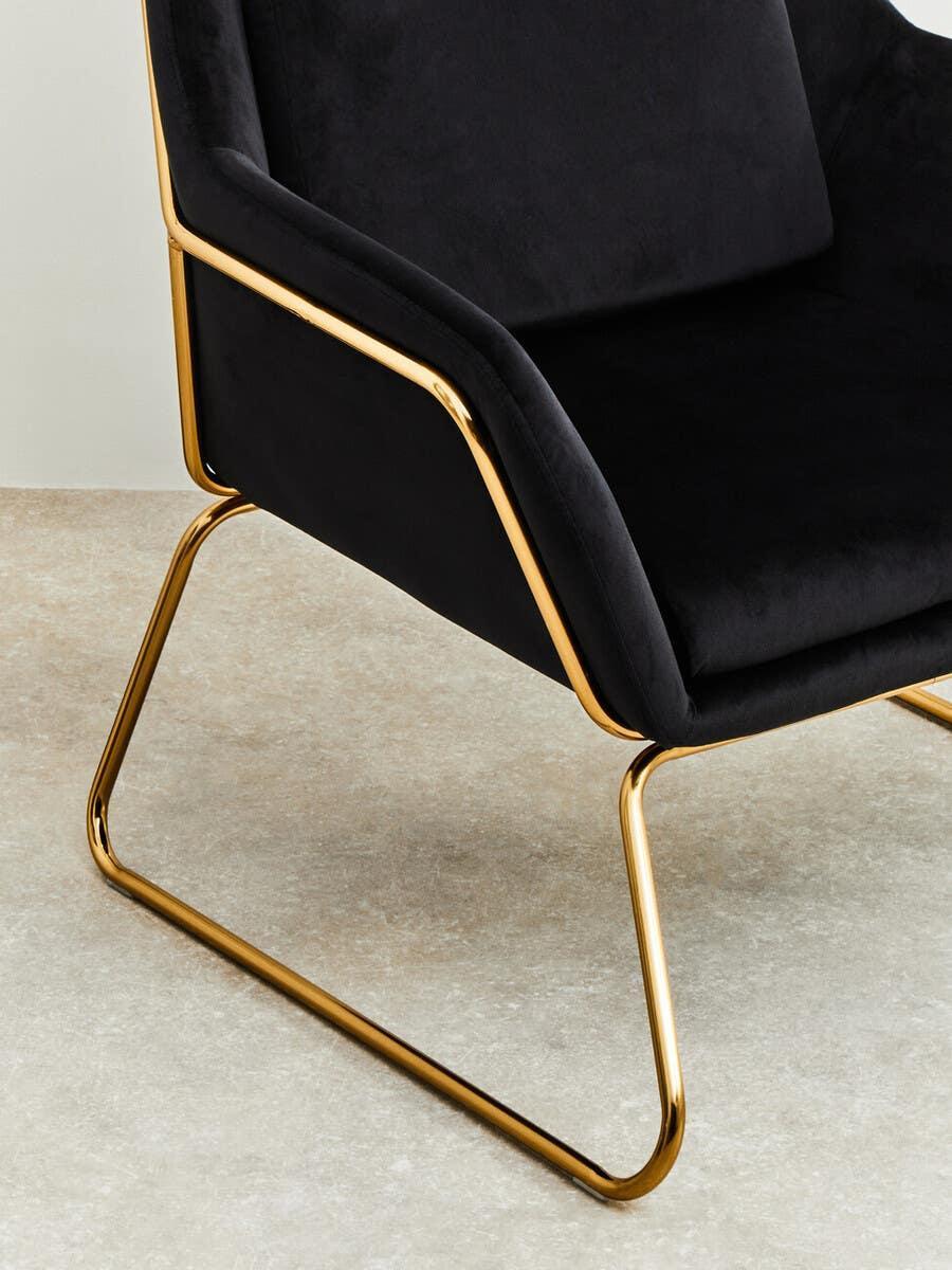 Black velvet accent chair with gold metal frame and modern angular design on stone floor