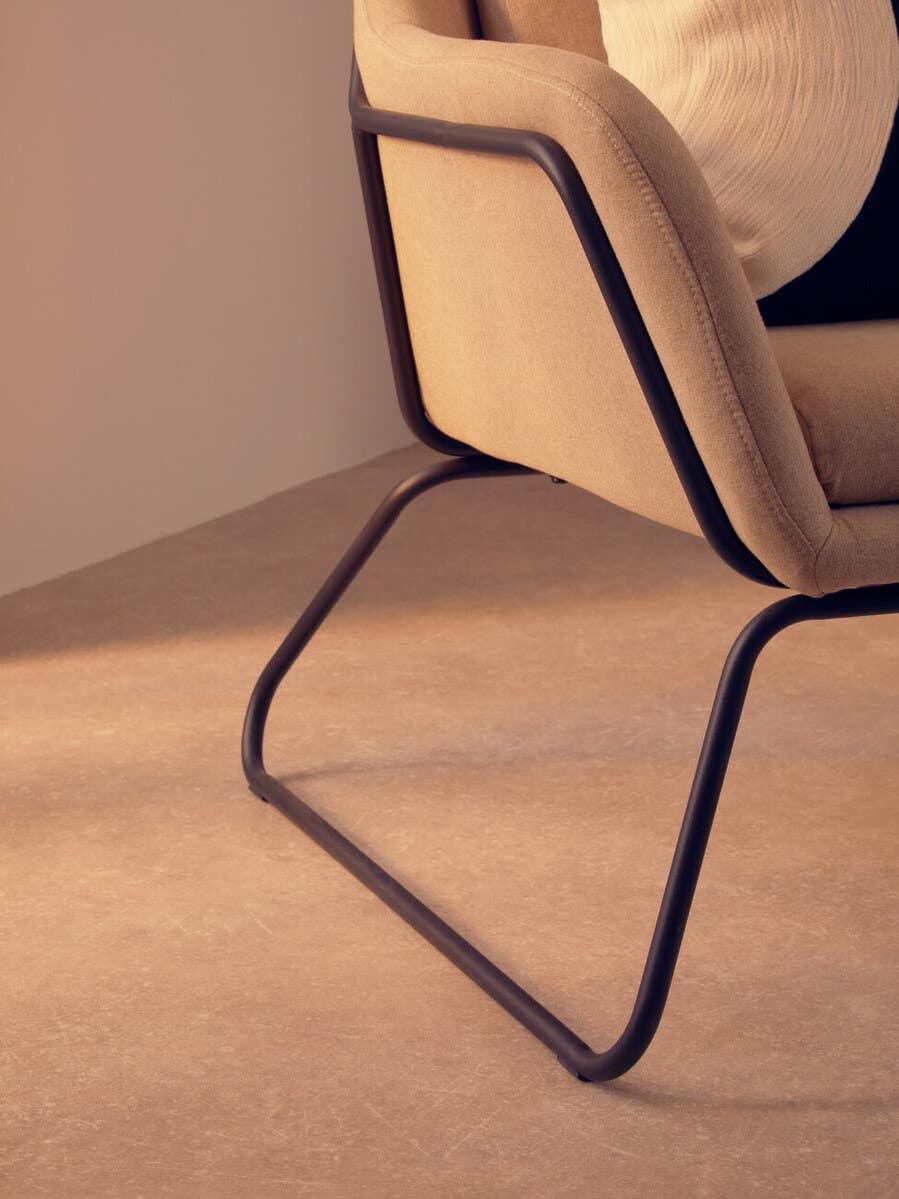 Closeup of beige upholstered chair with black metal frame on light flooring