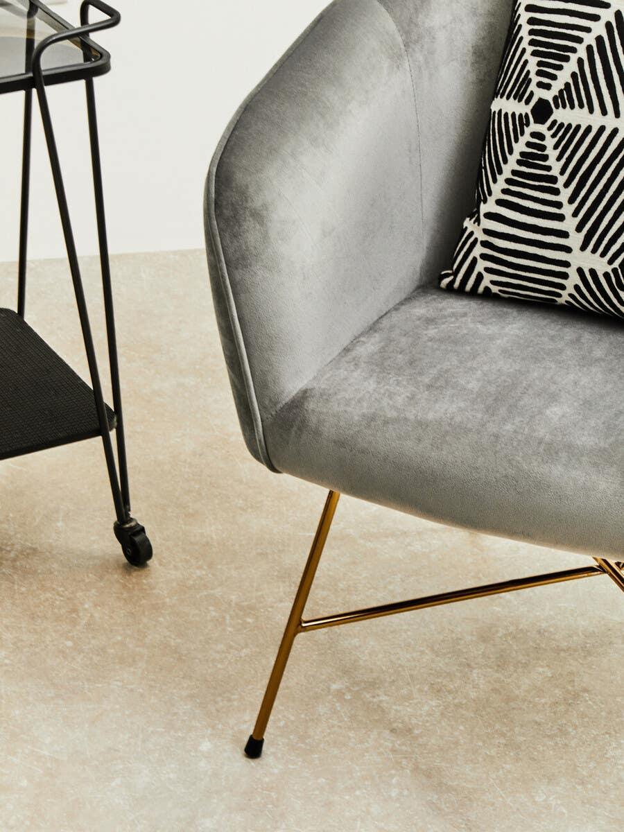 Grey velvet accent chair with gold legs and geometric black and white cushion