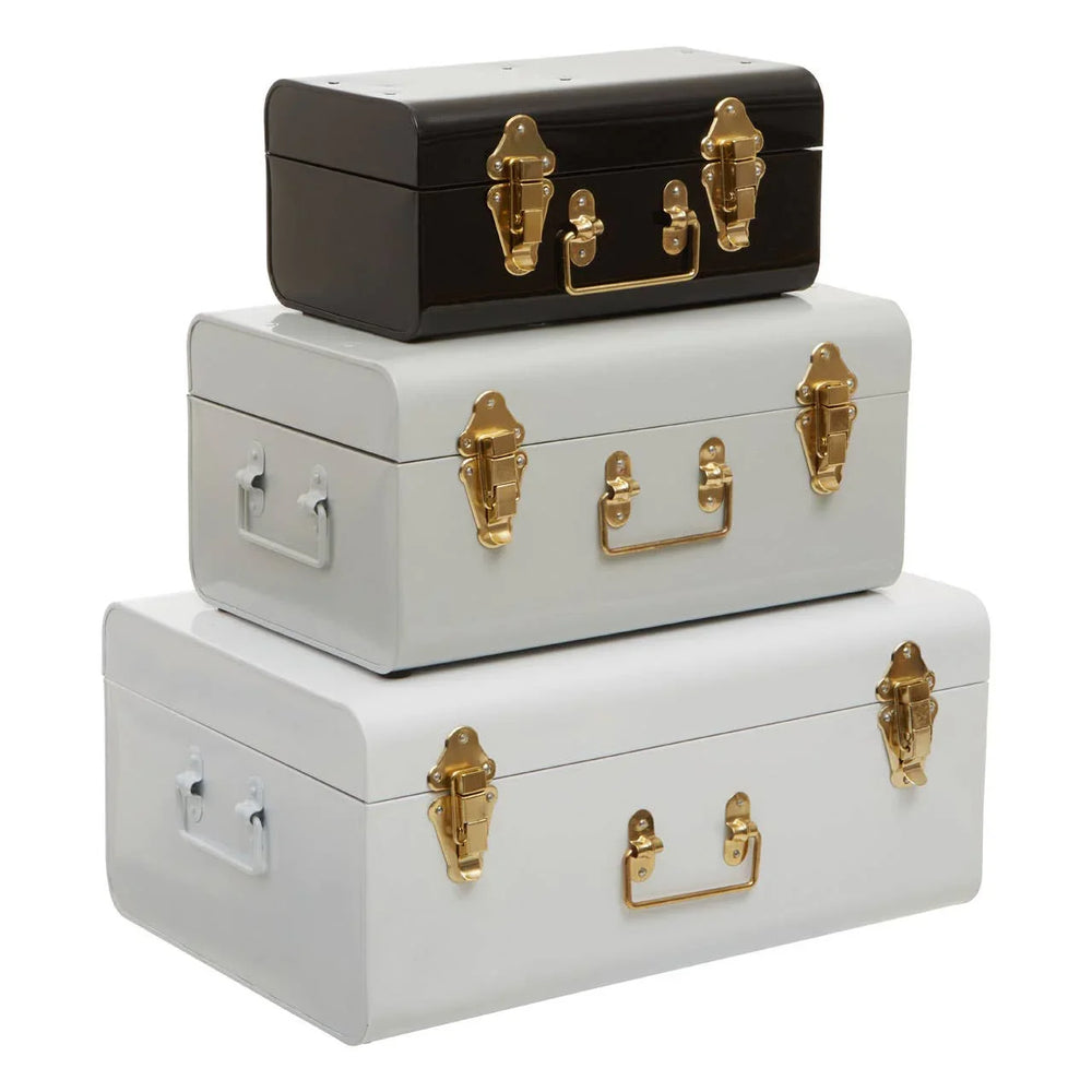 Set of three metal storage trunks in black, grey, and white with gold latches and handles