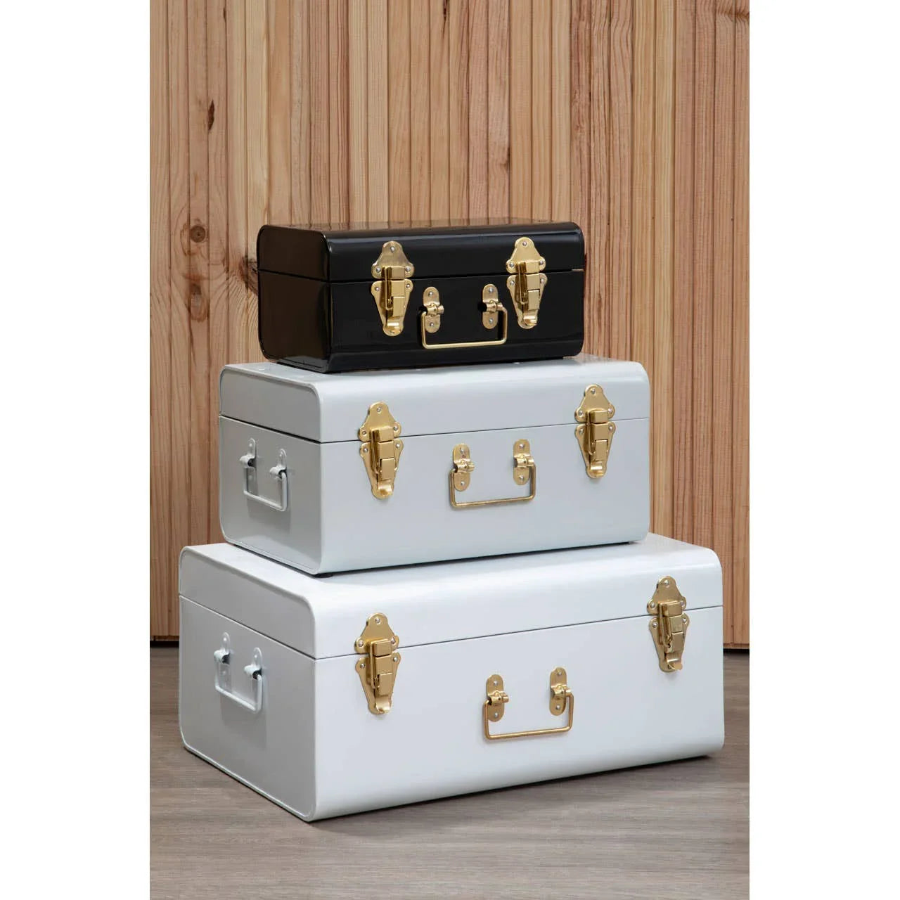 Set of metal storage trunks in black, white, and grey with gold clasps stacked on wood floor