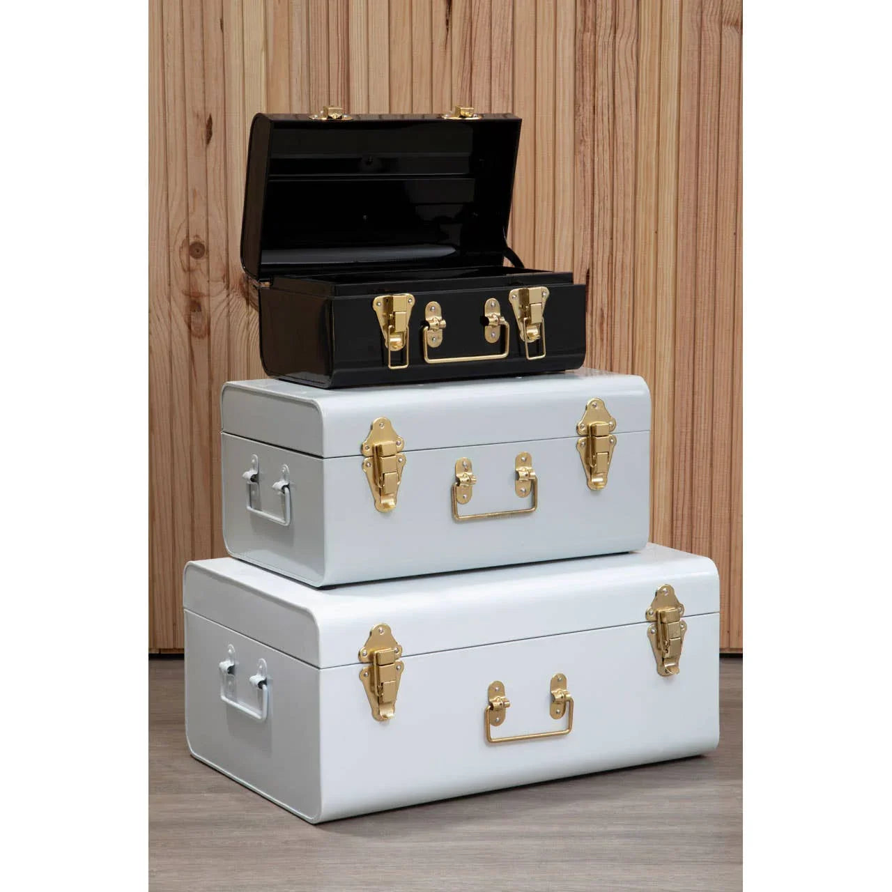 Set of three metal storage trunks with gold handles, stacked on wood floor
