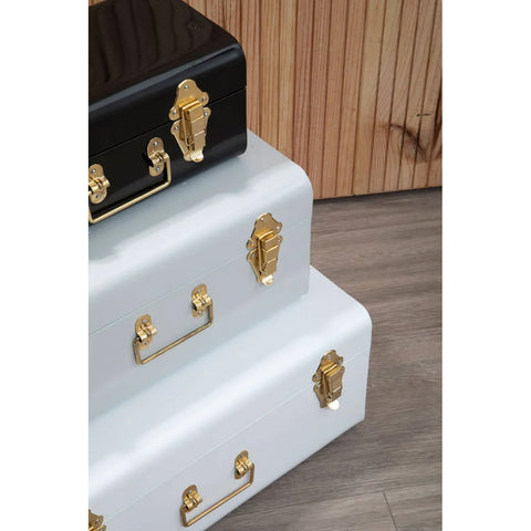 Stacked metal storage trunks in black and white with gold handles and clasps on wood floor
