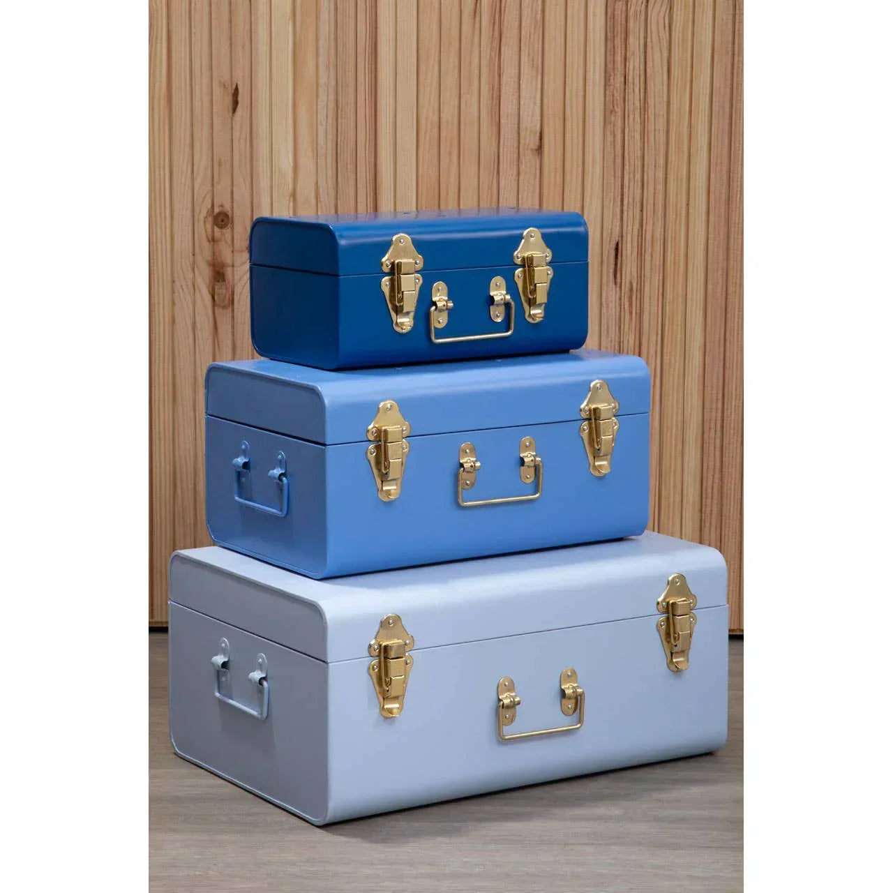 Set of three blue metal storage trunks with gold latches stacked on wood floor