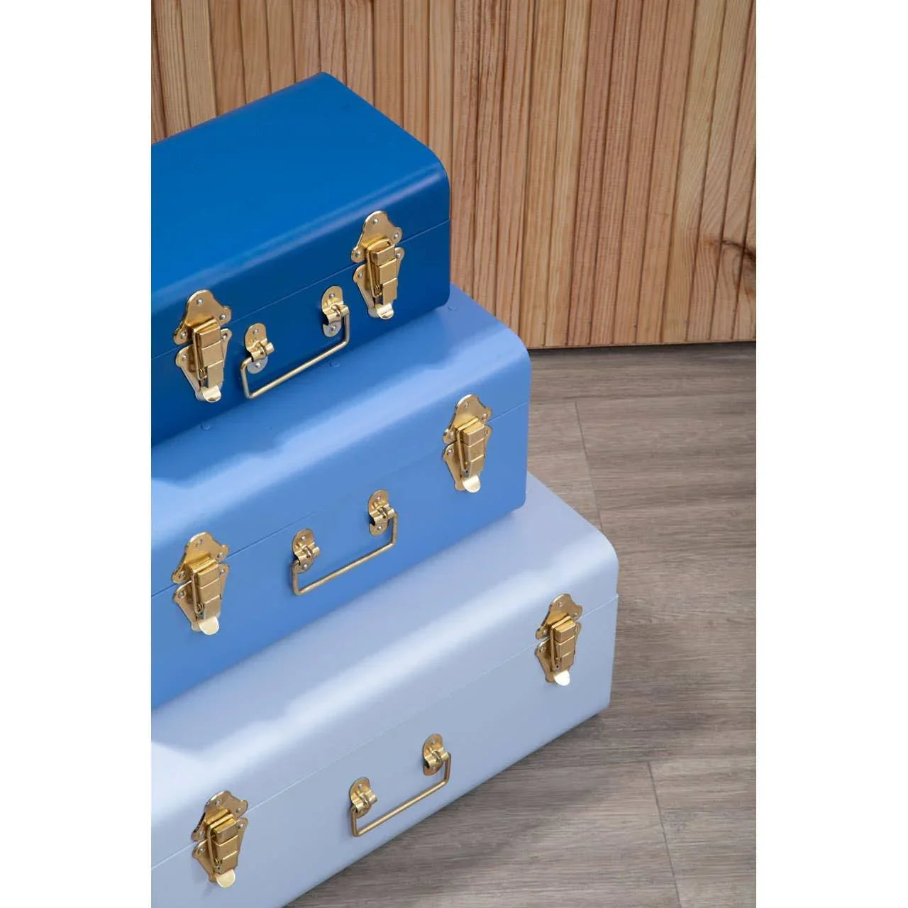 Set of three metal storage trunks in blue tones with gold clasps on wood floor
