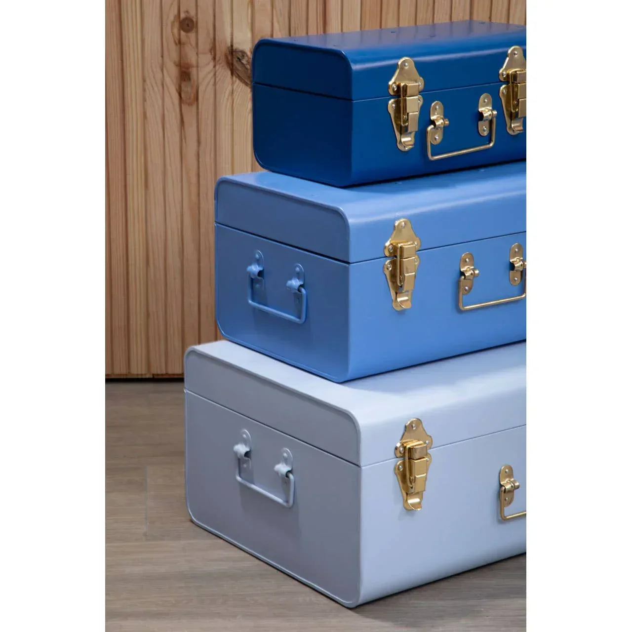 Stacked metal storage trunks in blue tones with gold latches against wooden panel wall