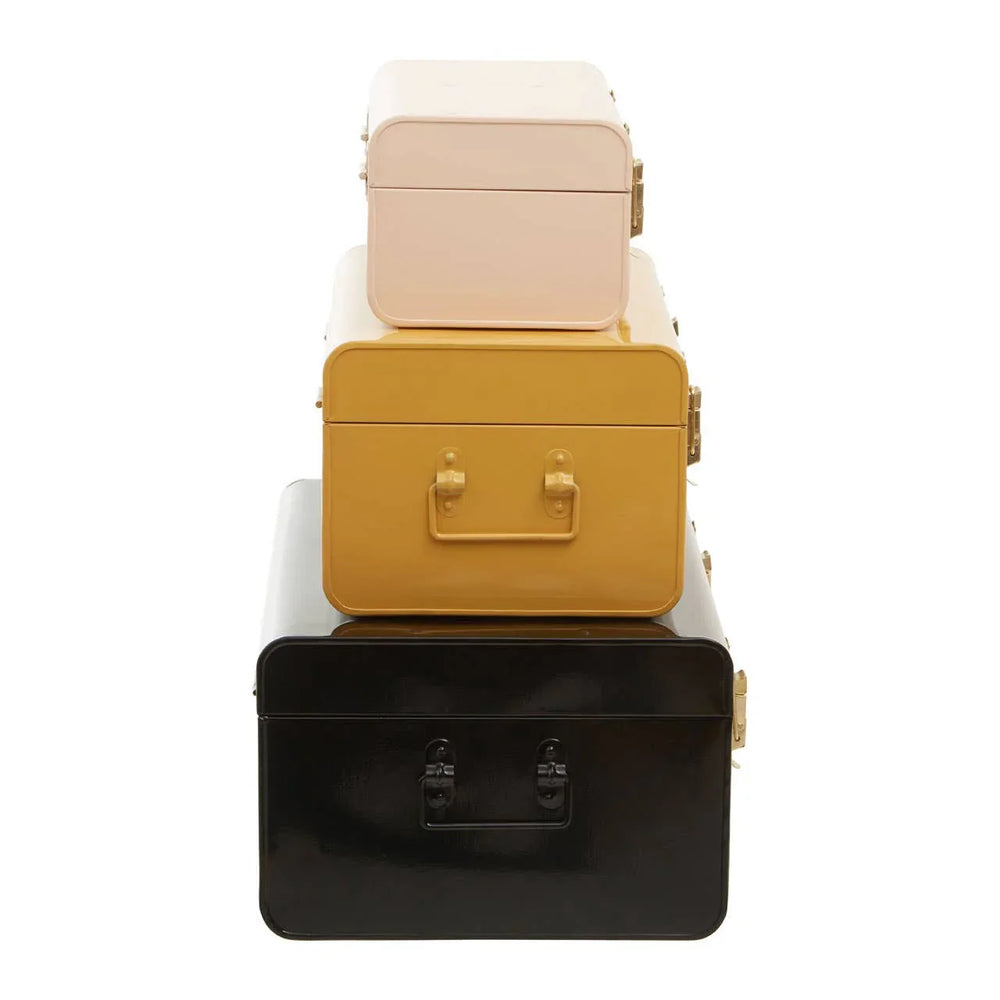 Set of three metal storage trunks in cream, mustard, and black stacked on white background