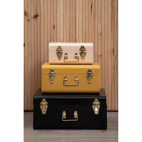 Set of three metal storage trunks in pink, yellow, and black with gold clasps on wood floor